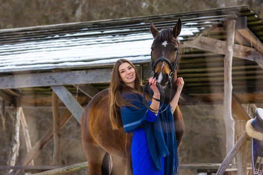 A girl in a blue dress hugs a horse against the backdrop of a snow-covered canopy in the forest a