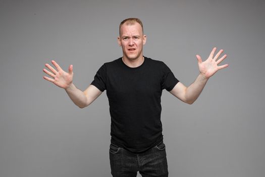 Portrait of dissatisfied angry blond Caucasian man in black holding his arms outstretched showing disapproval and asking to stop it.