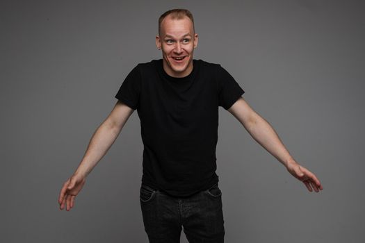 picture of caucasian man keeps his hands to the sides and looks to the camera isolated on grey background