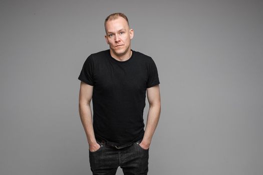 Portrait of Caucasian blond man in black clothing showing disbelief shrugging his shoulders and pointing at camera with his hand asking what is the problem.
