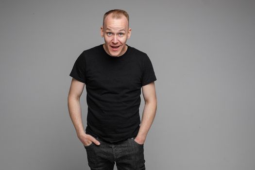 Surprised Caucasian man in black looking at camera with smile with hands on his waist.