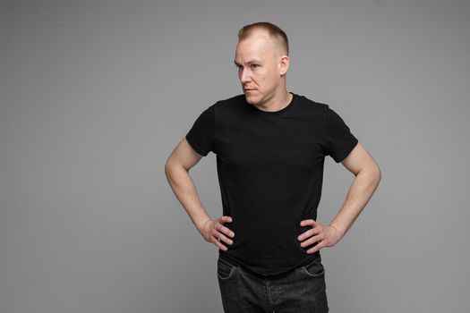 Surprised Caucasian man in black looking at camera with smile with hands on his waist.