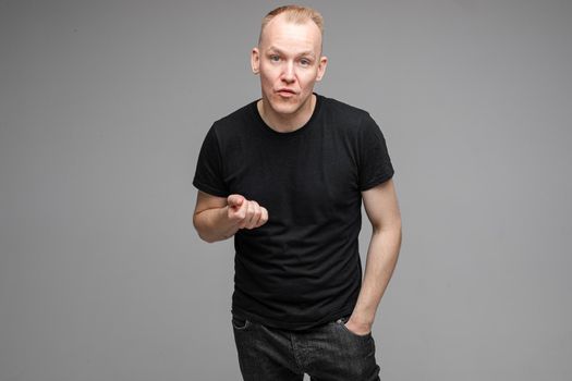 Waist-up photo of adult man in black shirt making a beaconing gesture with his hand and looking at the camera