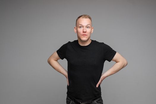 picture of handsome caucasian male keeps his hands on the belt and looks aside isolated on grey background