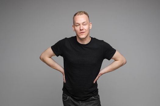 picture of handsome caucasian male keeps his hands on the belt and looks aside isolated on grey background