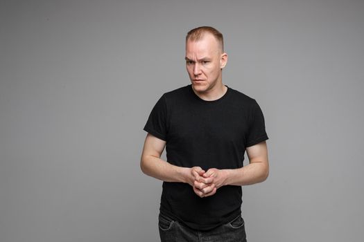 picture of handsome caucasian male keeps hands together looks with surprised sight isolated on grey background
