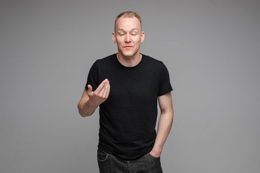 picture of handsome caucasian male keeps hands together looks with surprised sight isolated on grey background