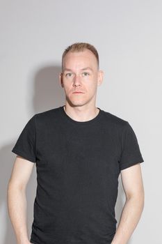 Studio portrait of emotionless blond Caucasian man in black t-shirt looking at camera. Isolate on white background.