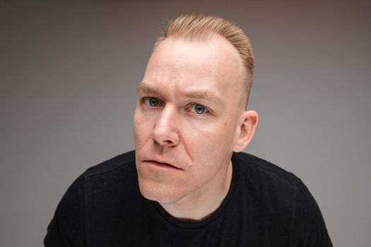 picture of handsome caucasian man in black t-shirt and short fair hair looks at something interesting in the camera