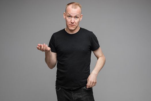 Portrait of Caucasian blond man in dark clothes outstretching his arms while showing his tongue at camera with wide open eyes. Cutout on grey background.