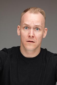 Portrait of frightened Caucasian man with blue eyes wide open looking at camera and asking for help. Cutout on grey.