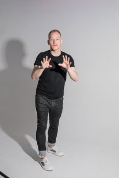 Full-length photo of man in black clothes raising his hands and opening mouth while posing at studio