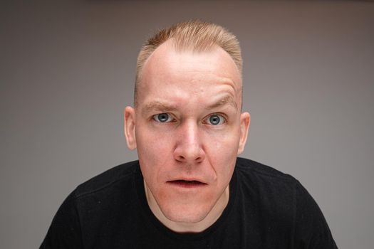 Portrait of confused blond Caucasian man with eyebrow up looking at camera in disbelief and confusion.