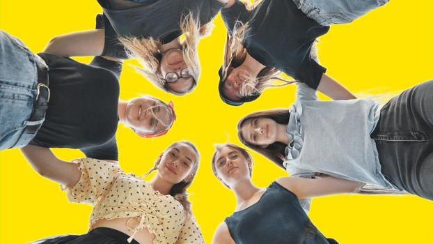 Happy girls friends hugging in a circle on a yellow background