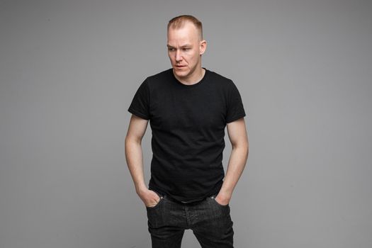 Portrait of Caucasian blond man in black clothing showing disbelief shrugging his shoulders and pointing at camera with his hand asking what is the problem.