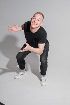 Full length of adult Caucasian blonde man in black t-shirt, dark jeans and sneakers talking to camera with arms bent, holding fists. Presenter or advertiser promoting something.