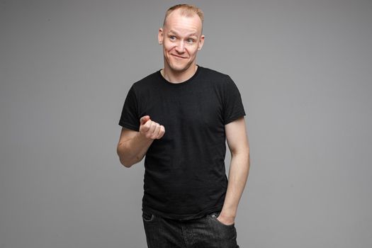 Waist-up photo of adult man in black shirt making a beaconing gesture with his hand and looking at the camera
