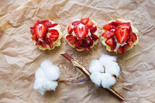 Beautiful cupcakes with strawberries along with a branch of cotton lies on kraft paper.