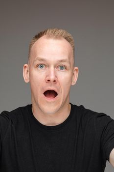 adult caucasian man in black t-shirt and short fair hair looks to the camera with an open mouth