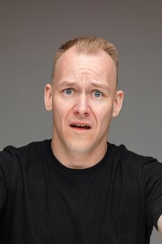 adult caucasian man in black t-shirt and short fair hair looks at something digust