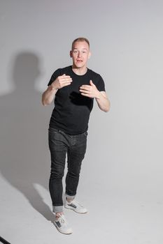 Full-length photo of man in black clothes raising his hands and opening mouth while posing at studio