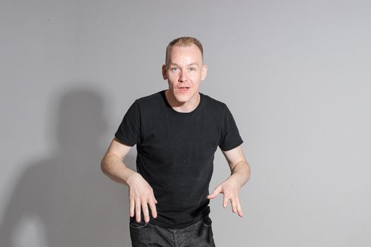 funny man keeping his hands up and smiles in studio on white background, backstage of a photosession