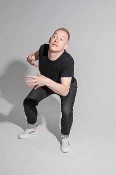 Full length of adult Caucasian blonde man in black t-shirt, dark jeans and sneakers talking to camera with arms bent, holding fists. Presenter or advertiser promoting something.