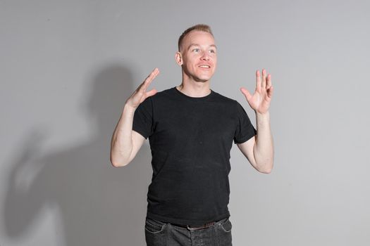 Waist-up photo of expressive man in black shirt crossing his hands while posing at professional studio