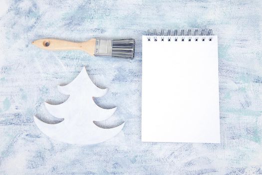 Shabby chic flatlay with brush, pine tree and notepad with white sheet on craft painted background