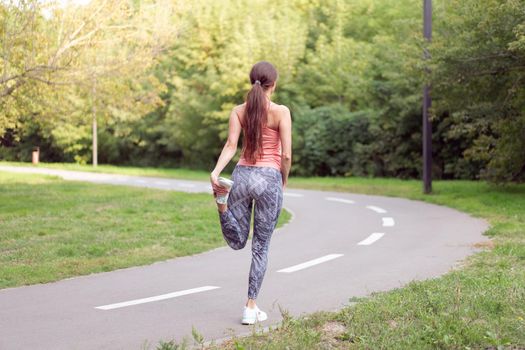 Athletic woman warming up legs before running exercises standing running track in summer park Morning cardio training Middle age caucasian female warm up body before jogging asphalt path in public park
