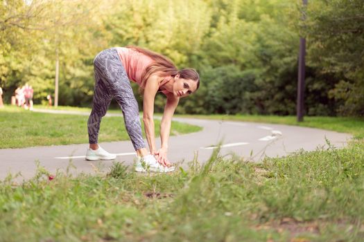 Athletic woman warming up legs before running exercises standing running track in summer park Morning cardio training Middle age caucasian female warm up body before jogging asphalt path in public park