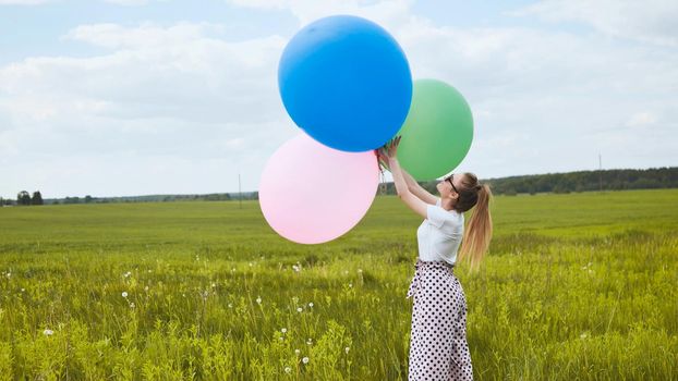 Happy girl with big multicolored balloons posing on the field