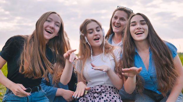A group of girls of friends are listening to music on headphones and dancing to a friend