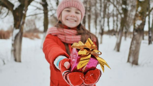 The charming young schoolgirl joyfully holds in her hands a packaged box with a gift in the winter forest. In anticipation of the New Year holidays