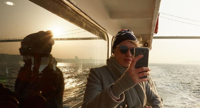 Young amazing woman outdoors on boat in sea take a selfie by mobile phone. Spring