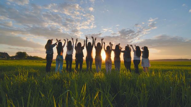 Silhouette of friends of 11 girls waving their hands at sunset in the field