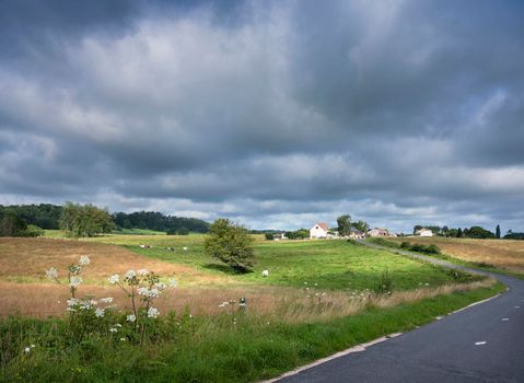 rural countryside summer landscape with green meadows and village in french ardennes near charleville under cloudy sky in france