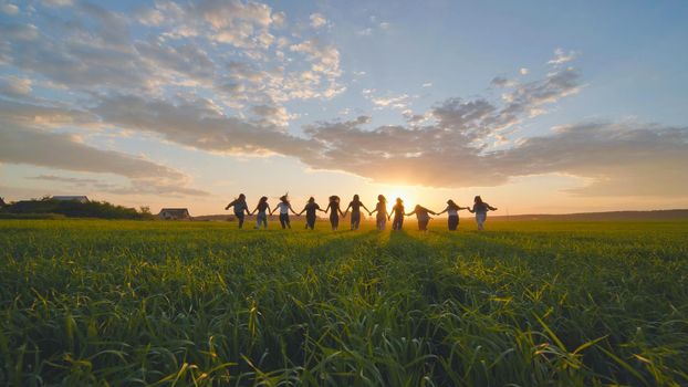 Eleven cheerful girls run to the meeting across the field in the summer, holding hands