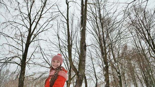 A young schoolgirl joyfully throws a snowball and breaks it with a palm when it falls. Emotions of joy. Winter fun in nature in the forest