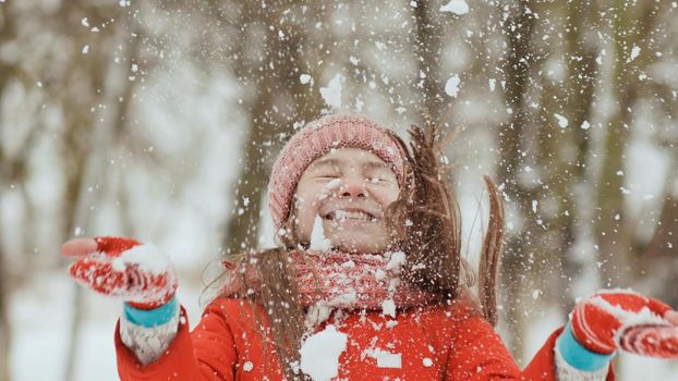 A young schoolgirl joyfully throws a snowball and breaks it with a palm when it falls. Emotions of joy. Winter fun in nature in the forest