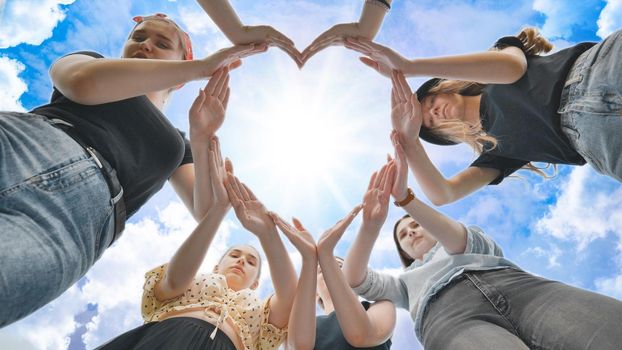 Girlfriends girls make a heart shape from their hands against the blue sky