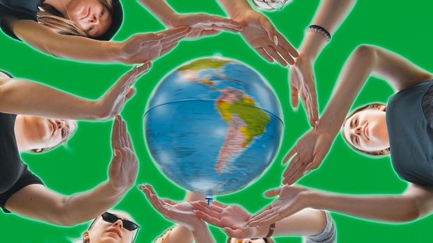 Schoolgirls hug the earth globe with their hands, making a circle out of them on a green background