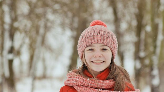 A young schoolgirl joyfully throws a snowball and breaks it with a palm when it falls. Emotions of joy. Winter fun in nature in the forest