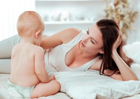 happy mom talking to the baby lying on the bed . the concept of education