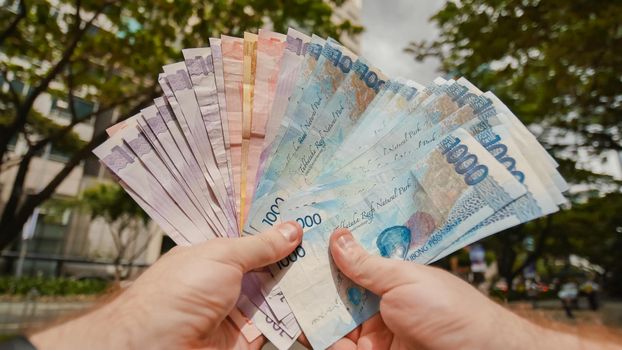 Photo of hands holding bundle of blue money in cash of one thousand philippines peso as if being rich, boastful. Show off, pay bills or give bribe. Payment procedure