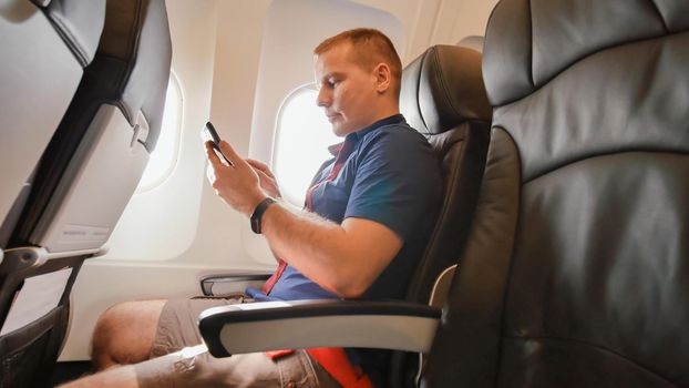 A young man in an airplane before a flight communicates on a mobile phone