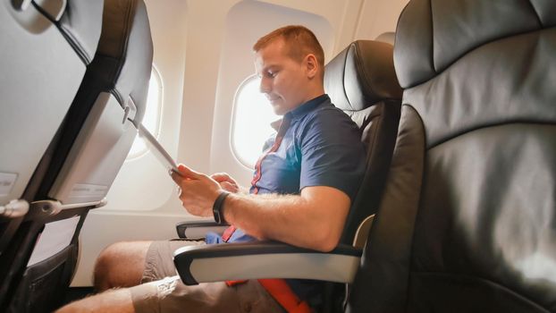 A young tourist on the plane works with the tablet before leaving