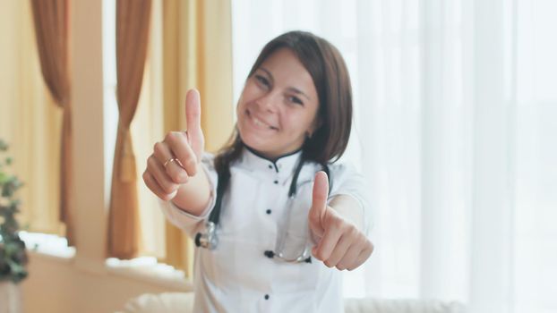 Portrait of a young female doctor in a good mood who shows thumbs up