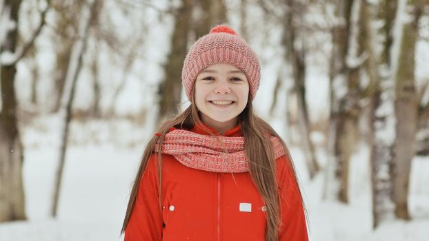 A teenage girl with freckles on her face happily smiles into the camera. A background of a winter forest landscape