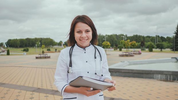 Young girl doctor walking down the street with documents and smiling